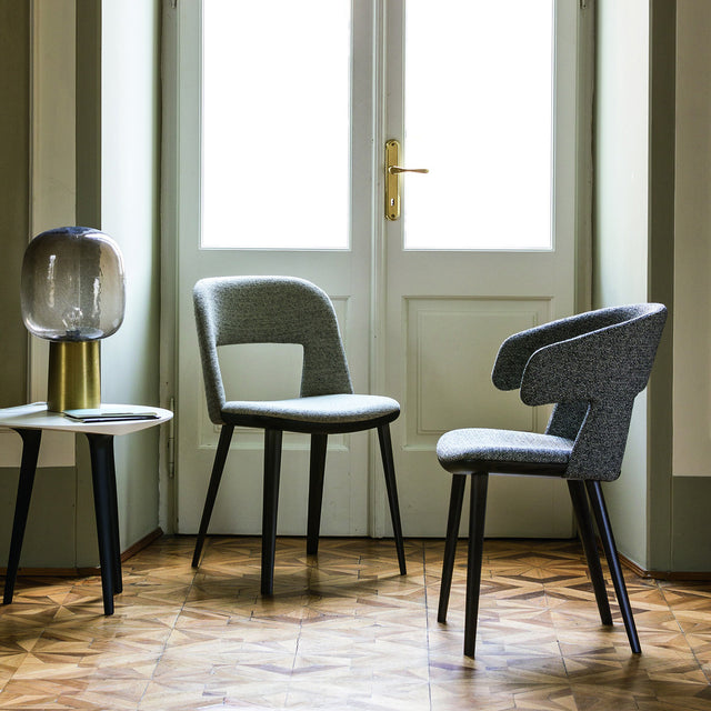 Path dining chair and armchair in upholstered fabric with open-back design, shown in a contemporary interior with wood flooring and soft natural light.