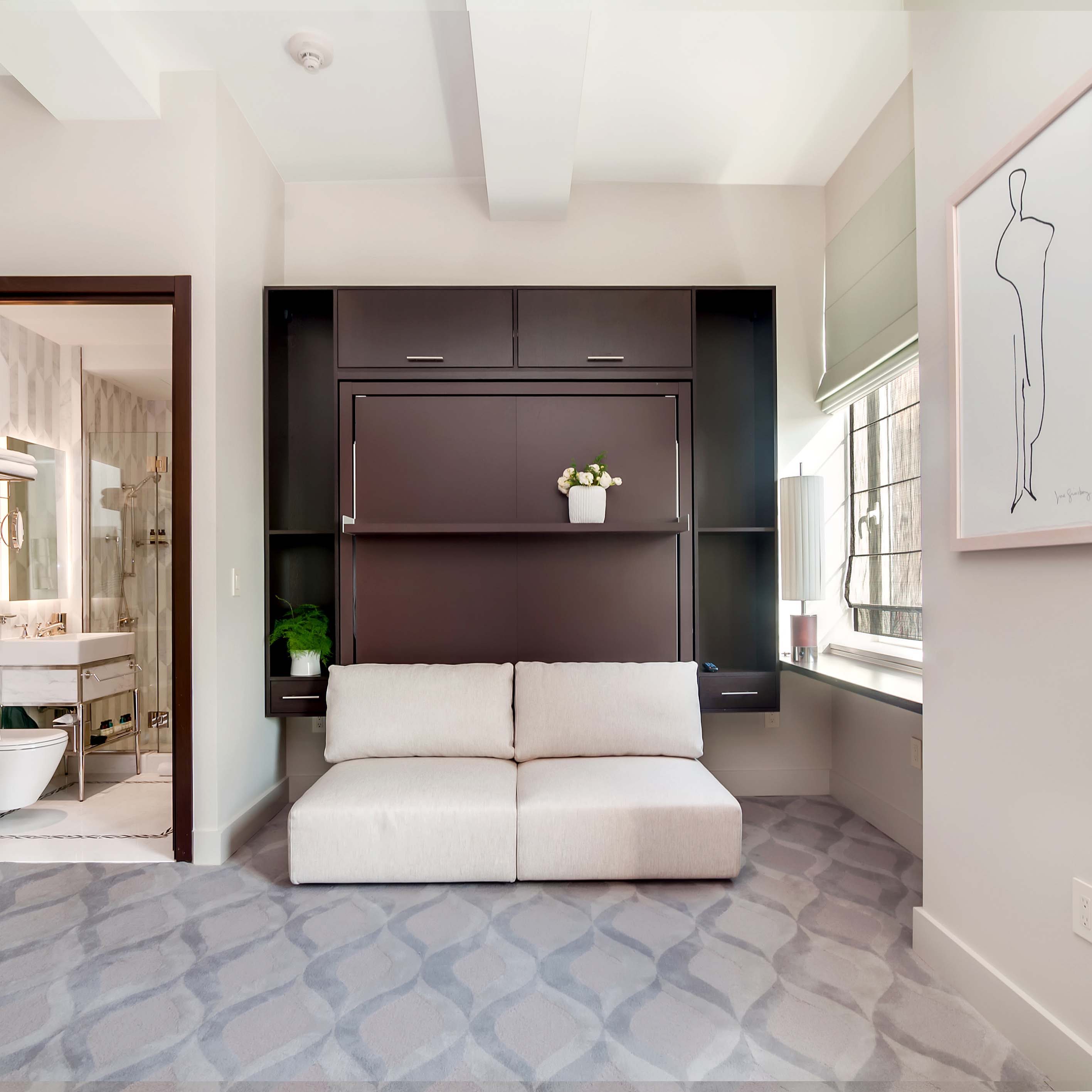 Swing 0 wall bed closed with soft beige sofa and built-in dark wood shelving in modern guest suite.